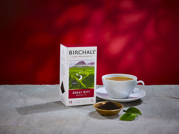 front lifestyle view of Birchall Great Rift prism Tea bags. On stone shelf, deep red background, brewed tea in white cups and a small bowl of tea leaves