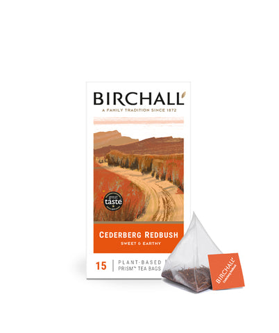 Front view of cardboard box of 15 Birchall Organic Redbush prism tea bags. Orange hill graphics with orange band, sweet & earthy, natural infusion. Caffeine free. Great Taste winner 2014 with one prism teabag on display next to box