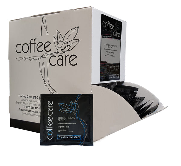 A Coffee Care dispenser box of 100 packets of 15g Three Peaks Blend cafetiere coffee. A white dispenser box with 1 cafetiere sachet lent up next to it.